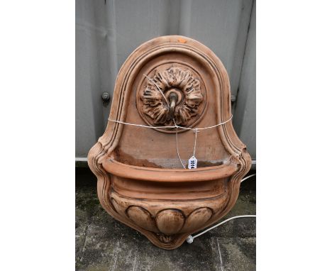 A TERRACOTTA WALL MOUNTED WATER FEATURE, with foliate detail surrounding the spout, which pours into a demi lune basin, fitte