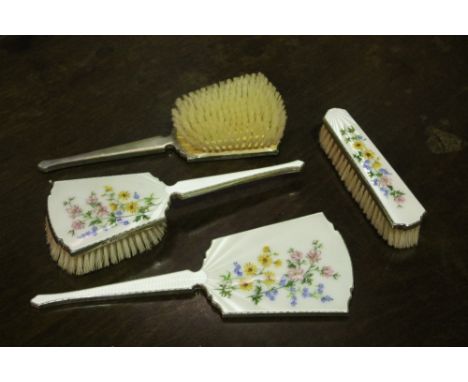 A FOUR PIECE DRESSING TABLE SET comprising three brushes and one mirror, with silver mounts and white enamel decoration with 