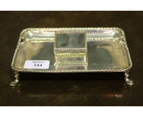 A SILVER INK STAND of rectangular form with raised fitted inkwell, on swept supports and with gadroon borders, London 1906 by