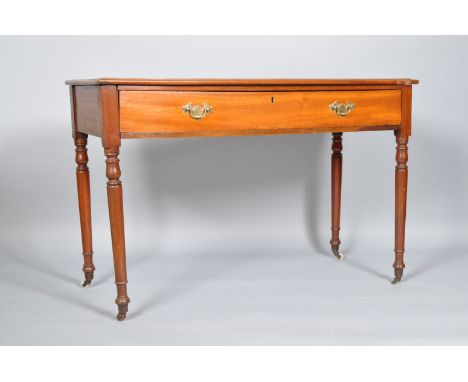 A mahogany desk, of plain rectangular form, with shaped edge, over a frieze drawer, with brass handles, raised on turned legs