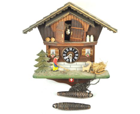 A 20th century Cuckoo clock of Swiss Chalet exterior form the doors opening to reveal a cow, with two fir cone moulded weight