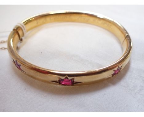 UNMARKED YELLOW METAL BANGLE, set with three 'garnets', concealed clasps and safety chain