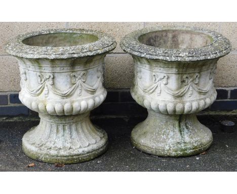 A pair of concrete garden urns, of semi fluted form, decorated with a band of repeating tied bows, 63cm high, 61cm wide.