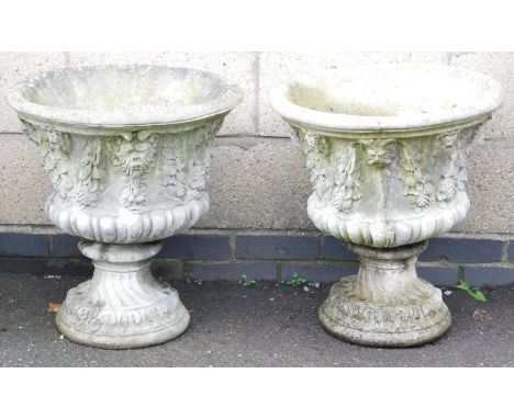 A pair of concrete garden urns, of semi fluted form, moulded with swags and leaves, 58cm high, 53cm wide.