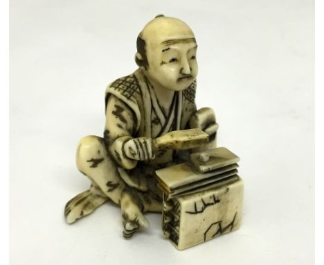 A Meiji Period Ivory Figure:Carved as a seated man in robe with bellows and set of drawers holding a fan.Height 4 cm