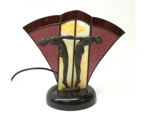 An Art Deco style table lamp, modelled in the form of two nude figures before a leaded purple and cream fan shaped glass shad