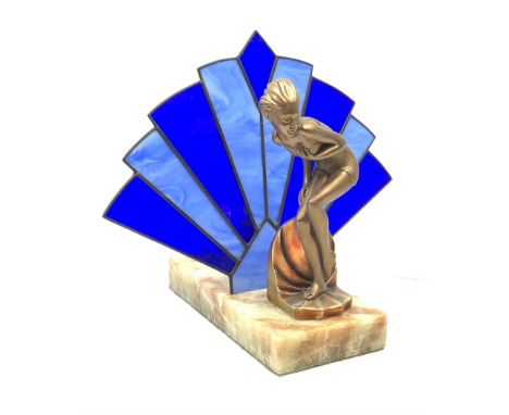 An Art Deco style table lamp, modelled in the form of a bronzed female figure before a leaded blue glass fan shaped shade, up