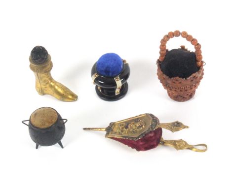 Five pin cushions, comprising a gilt brass example in the form of a set of bellows, 11.5cms, a coquilla nut pierced and carve