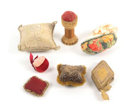 Seven pin cushions, comprising two formed from sea shells, largest 8cms, three cushion form material examples, a diamond form