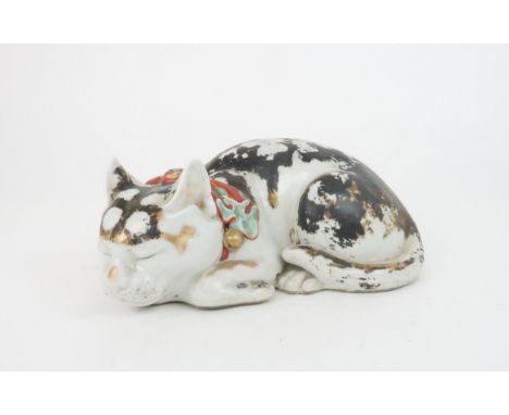 AN ARITA MODEL OF A RECUMBENT CAT asleep and wearing a red patterned bow and gilt bells, the body with mottled black and red 