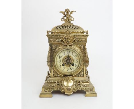 A FRENCH BRASS MANTLE CLOCK with cherub finial and central mask above the dial, the dial with arabic numerals, with pierced s