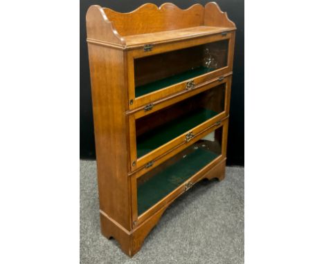 An Arts and Crafts oak three tier bookcase, three-quarter galleried top, above three glazed lift-up and slide doors, with bra