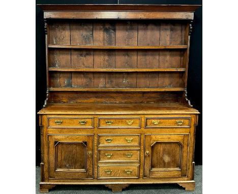 A George III revival oak dresser, the out-swept cornice above three tiers of plate-rack shelving, with plank back, and shaped