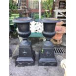 A pair of Victorian style black painted cast iron campana shaped garden urns, on square plinths,