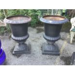 A pair of Victorian style black painted cast iron campana shaped garden urns, on square plinths,