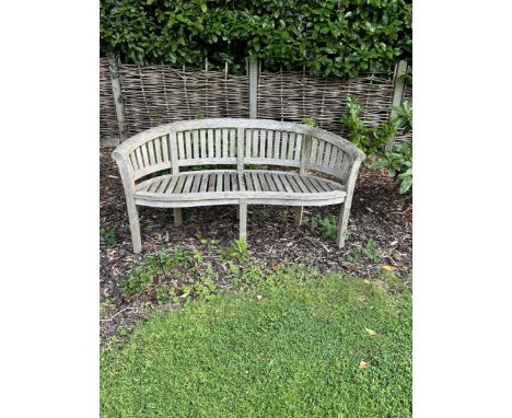 A curved teak bench, 160cm, 82cm high. Condition - weathered, otherwise good