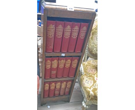 A small polished oak three shelf open bookcase containing fifteen vols. The Works of Charles Dickens 8v., red gilt boards, il