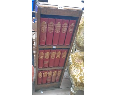 A small polished oak three shelf open bookcase containing fifteen vols. The Works of Charles Dickens 8v., red gilt boards, il