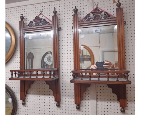 A pair of Edwardian walnut framed wall mirrors, each with decorative pediment and spindle gallery to shelf