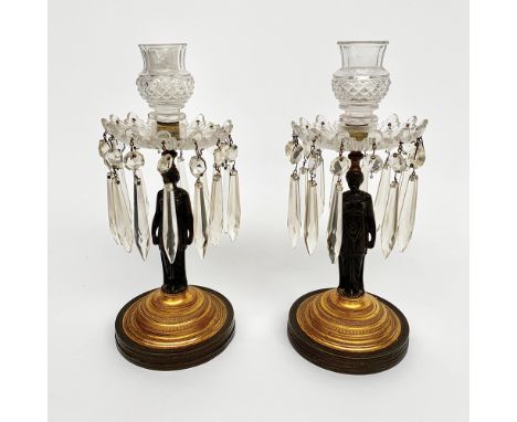 A pair of Regency bronze and gilt figural lustre candlesticks, with cut glass sconces, drops and drip pans, the stems cast as