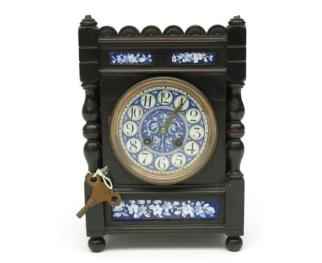 An Aesthetic movement ebonised oak mantel clock, with blue, black and white circular ceramic dial and three inset foliate pan