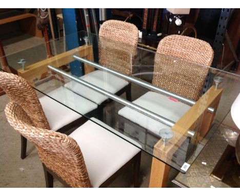 A light oak framed dining table with glass top 150 x 90cm together with four Wothaka raffia framed dining chairs 