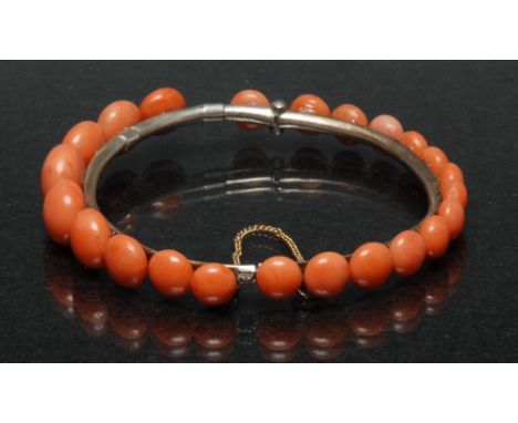 A coral mounted hinge bangle, two section hinged body mounted with twenty three graduated pink beads, unmarked tubular body, 