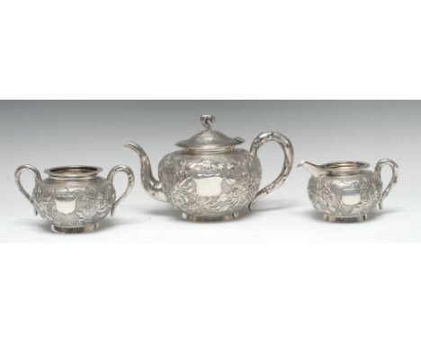 A Chinese silver three piece tea service, comprising teapot, milk jug and sugar basin, each chased with chrysanthemums on a t