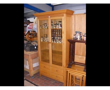 A modern light wood two door display cabinet with four drawers below 