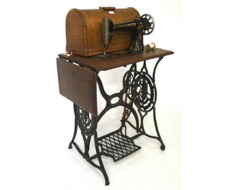 A vintage Singer sewing machine, the machine attached to a wooden top with a foldable end supported by a pierced metal frame 