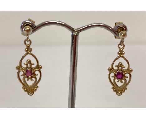 A pair of 9ct gold classic design drop style earrings, each set with a small round cut ruby. Full hallmarks to posts. Heart d