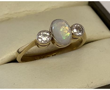 An 18ct gold and platinum opal and diamond dress ring. Central oval cut opal with a bezel set round cut diamond to each side.