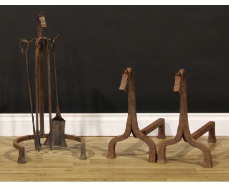 An Arts &amp; Crafts wrought iron zoomorphic fireside hearth suite, comprising a pair of andirons and a stand with shovel, po