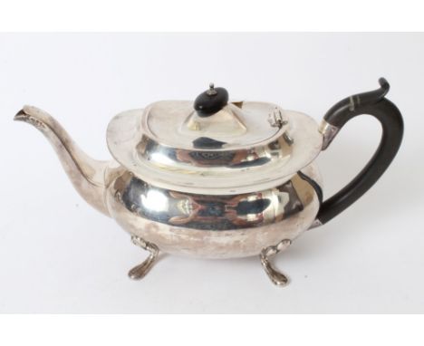 George V silver teapot of compressed baluster form, with ebony loop handle and hinged domed cover with ebony finial, on four 