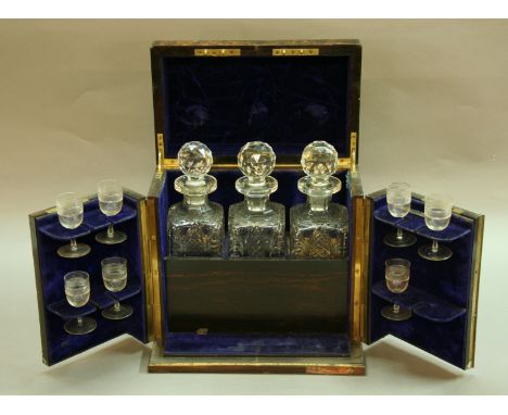 A VICTORIAN COROMANDEL DECANTER BOX the hinged lid and pair of doors enclosing three decanters and stoppers and a set of glas