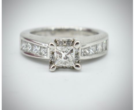 A 14ct white gold and diamond ring. The ring set with a princess cut diamond in prong mount flanked by diamond set channel sh