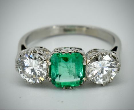 A platinum Colombian emerald and diamond three stone ring. The ring set with a central octagonal cut Colombian emerald flanke