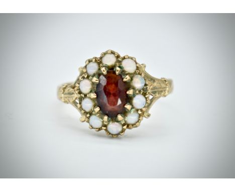 A 9ct gold opal and garnet cluster ring. The ring with central oval facet cut garnet within a halo of cabochon opals. Unmarke