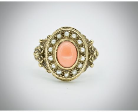 A hallmarked 9ct gold coral and pearl ring. The ring set with an oval coral cabochon surrounded by half pearls to foliate emb