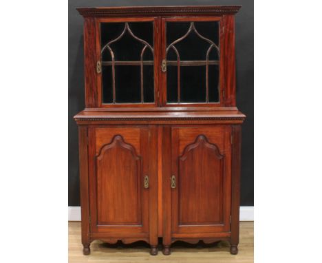 An unusual and composed mahogany library side cabinet, outswept meandrous cornice above a pair of glazed doors enclosing a sh