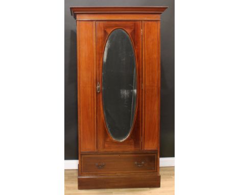 An Edwardian mahogany wardrobe, outswept cornice with faux-dentil parquetry apron above an oval bevelled mirror door enclosin