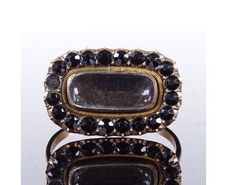 A Georgian unmarked gold memorial panel ring, central glass covered vacant hair panel surrounded by faceted jet with closed-b