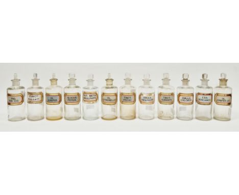 Twelve early 20th century 'label under glass' apothecary bottles and stoppers, each of cylindrical form with faceted rectangu