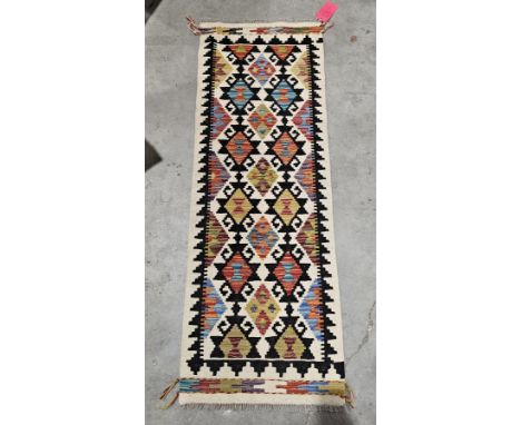 Chobi kilim runner, 20th century, woven in black, cream and bold palette with repeating foliate rosettes, within a black and 