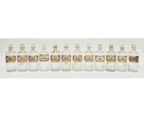 Twelve early 20th century 'label under glass' apothecary bottles, each of cylindrical form with faceted rectangular stopper, 