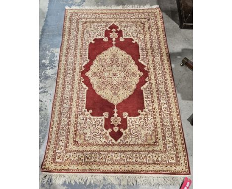 Persian rug with central cream, beige and red foliate medallion, on a red ground within cream, beige and red borders of scrol