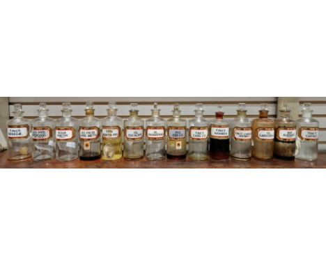 Fourteen small early 20th century 'label under glass' apothecary bottles and stoppers, each of cylindrical form with assorted