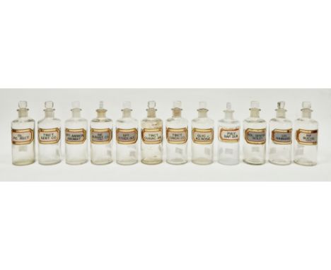 Twelve early 20th century 'label under glass' apothecary bottles, each of cylindrical form with faceted rectangular stopper, 