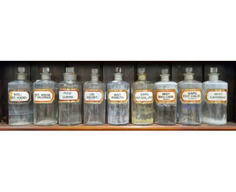 Nine large early 20th century 'label under glass' apothecary bottles and stoppers, each of cylindrical form with assorted fac