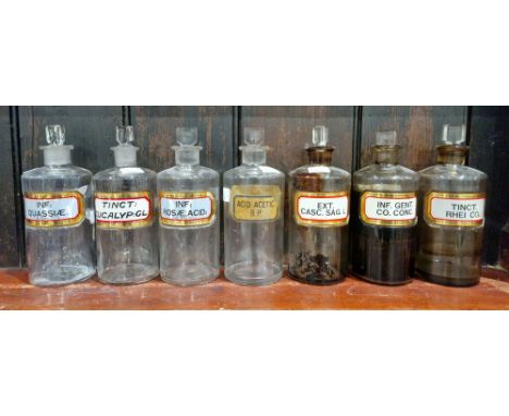 Seven early 20th century 'label under glass' apothecary bottles and stoppers, each of cylindrical form with assorted faceted 